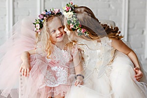 Portrait of two cute and beauty little girl - sisters in wreaths of fresh flowers have fun and smile in a bright studio. Close-up