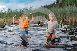 Portrait of two cute little boys standing at lake shore in the forest. one boy wearing life vest, another wearing armbands.