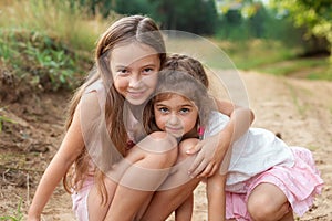 Portrait of Two Cute little girls embracing and laughing at the forest. Happy kids outdoors