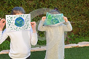 Portrait of the two cute little girls holding the drawing earth globe.Kids paintig picture of earth having fun outdoor.