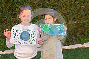 Portrait of the two cute little girls holding the drawing earth globe.Kids paintig picture of earth having fun outdoor.