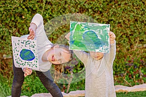 Portrait of the two cute little girls holding the drawing earth globe.Kids paintig picture of earth having fun outdoor.