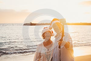 Portrait of two cute old persons having fun and enjoying together at the beach on christmas days at the beach wearing Christmas