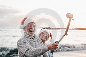 Portrait of two cute old persons having fun and enjoying together at the beach on christmas days at the beach wearing Christmas