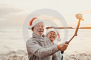 Portrait of two cute old persons having fun and enjoying together at the beach on christmas days at the beach wearing Christmas