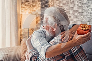 Portrait of two cute and old seniors at home having fun together. Mature man giving a gift at his wife for Christmas or