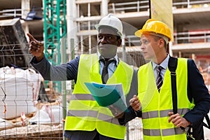 Portrait of two engineers in helmet and yellow vests. Indicate finger to side