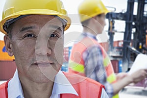 Portrait of two engineers in protective workwear working, looking at camera, outside in a shipping yard