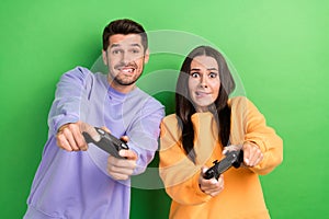 Portrait of two excited people biting lips try hard playing video games isolated on green color background