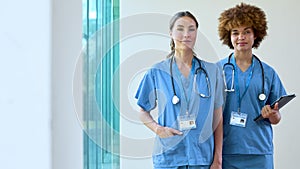 Portrait Of Two Female Doctors With Serious Expressions In Scrubs With Digital Tablet In Hospital