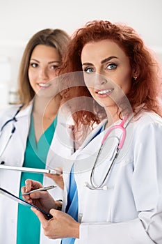 Portrait of two female doctors standing with clipboard and table