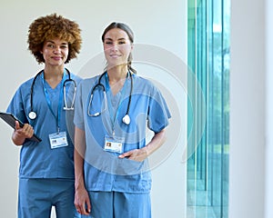 Portrait Of Two Female Doctors Wearing Scrubs With Digital Tablet In Hospital