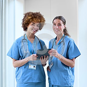 Portrait Of Two Female Doctors Wearing Scrubs With Digital Tablet In Hospital