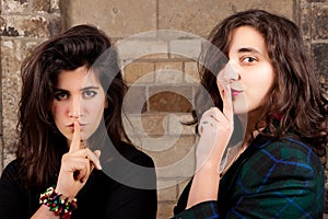 Portrait two female friends silencing finger mouth