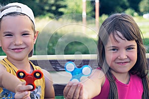 Portrait of two funny smiling friends playing with colorful fidget spinners on the playground. Popular stress-relieving