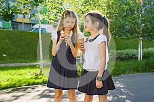 Portrait of two girlfriends schoolgirls 7 years old in school uniform eating ice cream.