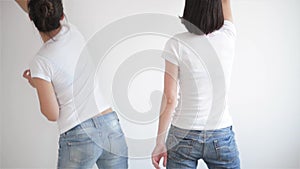 Portrait of Two Girls in Blue Jeans Making Repairs at Home with Platens. Back View of the Female Legs on White Wall