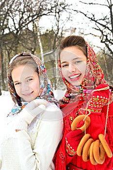 Portrait of two girls in bright shawls on a background of a winter forest during a winter holiday. Russian traditions