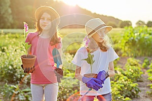 Portrait of two girls children with flowers in pots, gloves, with garden shovels