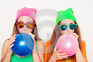 Portrait of two girls in hats and spectacles blowing balloons