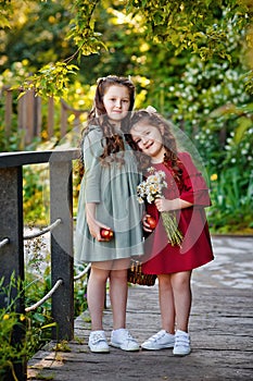 Portrait of two girls in a red and green dress, smiling outdoors, enjoying a warm sunny summer day. Sisters with apples and