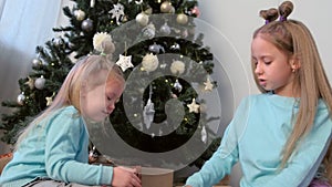 Portrait two girls sisters draw fingers on pillow sequins near Christmas tree.