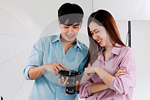 Portrait of two handsome man and beautiful woman wearing casual shirts and looking or checking pictures in camera while standing