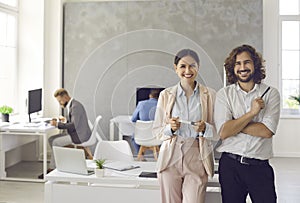 Portrait of two happy business partners of a woman and a man standing in a modern coworking center.