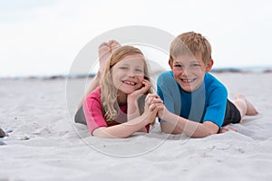 Portrait of two happy children in neoprene swimsuits playing on the beach with sand