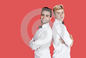 Portrait of two happy male friends in formals standing back to back over red background