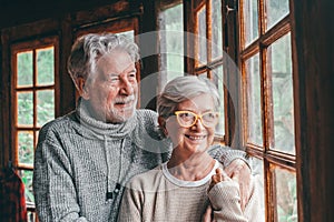 Portrait of two happy senior having fun together and looking outside the window at home. Close up of cute couple smiling and