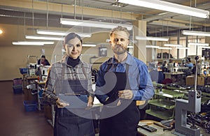 Portrait of two happy shoe factory workers standing in workshop and looking at camera