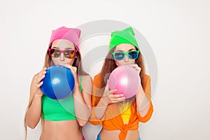 Portrait of two hipster girls in glasses blowing balloons