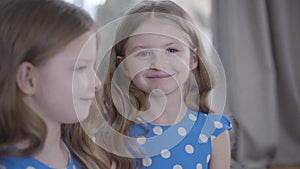 Portrait of two identical twin sisters with brunette hair and grey eyes smiling. Focused at face of happy child at the