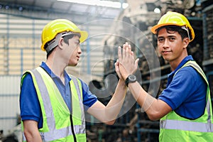 Portrait of two industrial engineer workers man wearing helmet doing high-five hand touch, standing at manufacturing plant factory