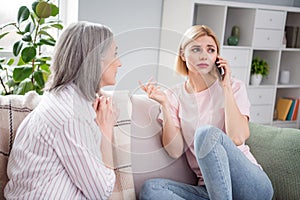 Portrait of two ladies sit on sofa speak phone interested listening information worry free time weekend indoors