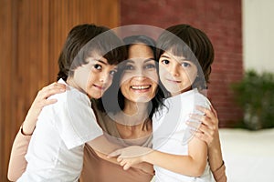 Portrait of two latin children, little twin boys smiling at camera and hugging their mom, spending time together at home