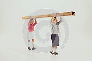 Portrait of two little boys, children carrying giant long box isolated over grey studio background. Playful kids