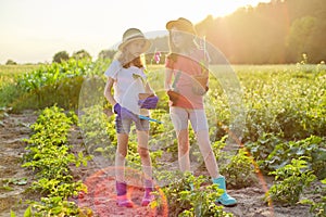 Portrait of two little gardeners in gloves with flowering plants in pots and garden shovels