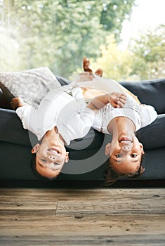 Portrait of two little mixed race siblings spending time together lying upside down at home. Cute hispanic girl and boy