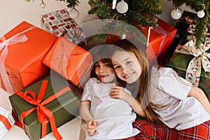 Portrait of two little sisters having fun and fooling around on Christmas morning near the Christmas tree.