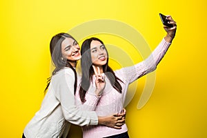 Portrait of two lovely girls dressed in sweaters standing and taking a selfie