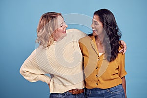 Portrait Of Two Mature Female Friends Laughing At Camera Against Blue Background