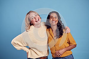 Portrait Of Two Mature Female Friends Laughing At Camera Against Blue Background