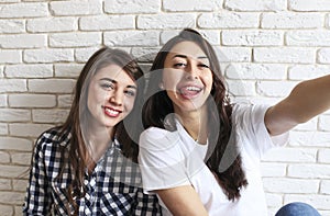 Portrait of two millennial females, fooling around in front of mobile smartphone camera. Brown eyed model girls with long brunette