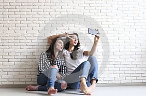 Portrait of two millennial females, fooling around in front of mobile smartphone camera. Brown eyed model girls with long brunette
