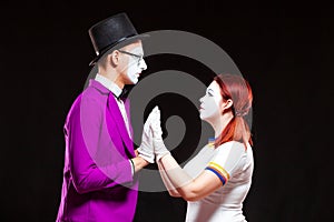 Portrait of two mime artist, isolated on black background. Young man and woman stand opposite touching palms and looking