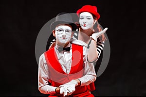 Portrait of two mime artists, isolated on black background. Woman appears from behind a man smiling. Symbol of happy
