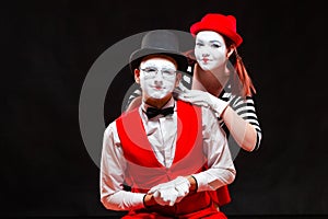 Portrait of two mime artists, isolated on black background. Woman appears from behind a man smiling. Symbol of happy