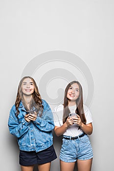 Portrait of two mixed race girls social network addiction on mobile phones isolated over graybackground